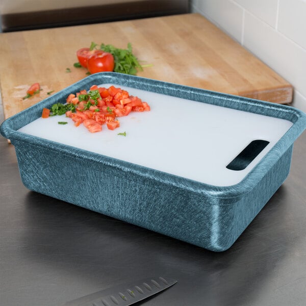 A blue HS Inc. cutting board in a blue container with white liquid and diced tomatoes on a counter.