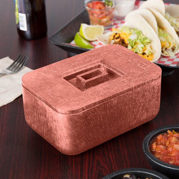 A HS Inc. metal container with a square hole on top and a lid on a table with a plate of tacos.