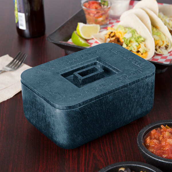 A blue rectangular HS Inc. multi-purpose container with a square lid on a table with a bowl of food.