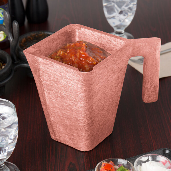 A HS Inc. Paprika pitcher filled with red salsa on a table in a Mexican restaurant.