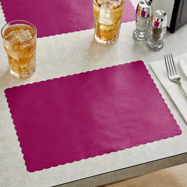 A wine colored scalloped paper placemat on a table with a glass of ice tea.