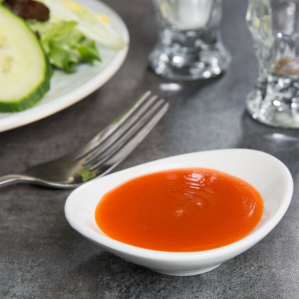 A pearl white Tuxton China ramekin filled with red sauce on a table next to a plate of salad.