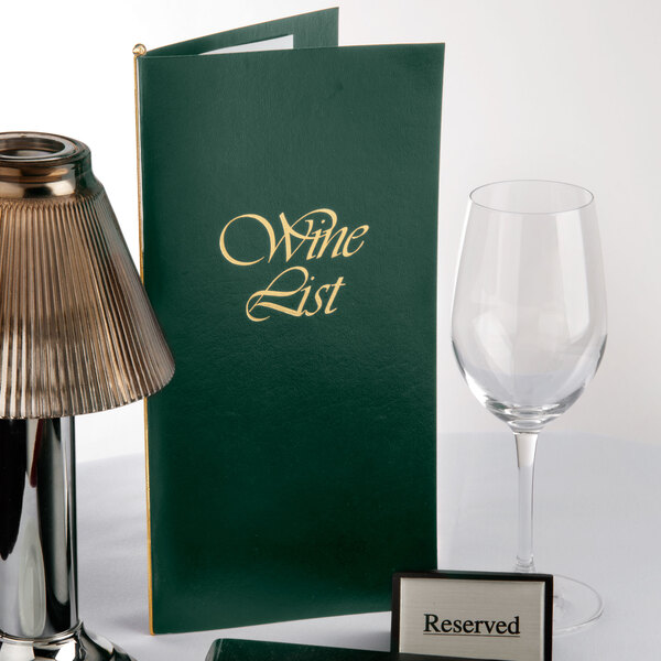 A green Menu Solutions wine list cover on a table with a glass of wine.
