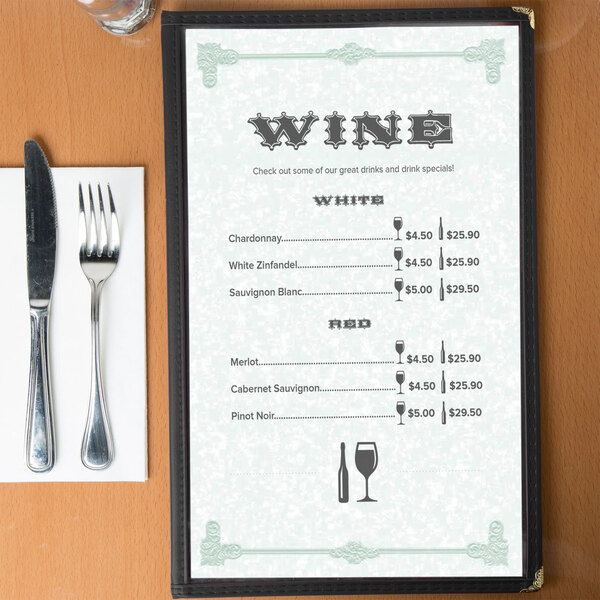 A green menu with a scroll border on a table with wine glasses and wine bottles.