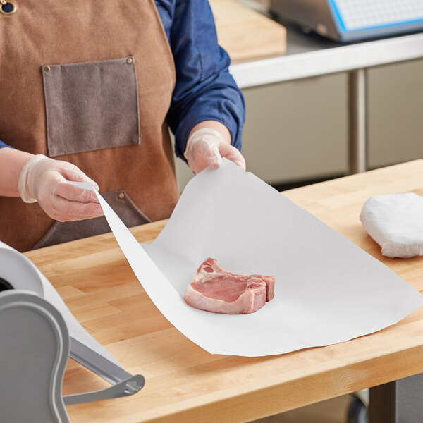 A person in a brown apron and gloves using Choice white butcher paper to wrap meat.