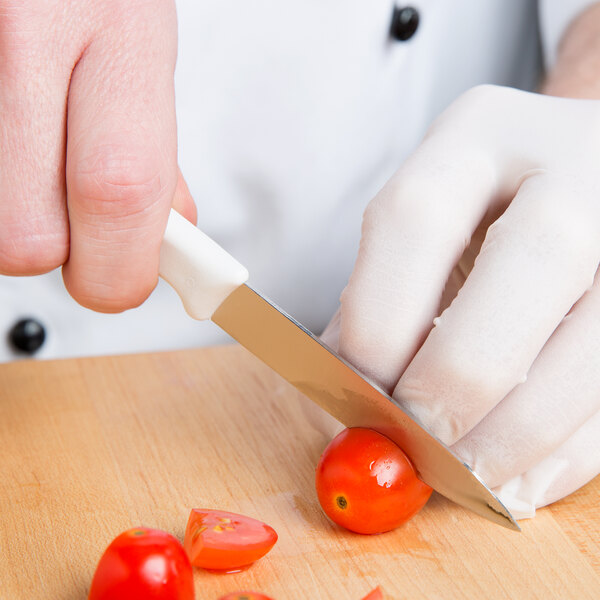 A gloved hand uses a Victorinox paring knife to cut a tomato on a wooden cutting board.
