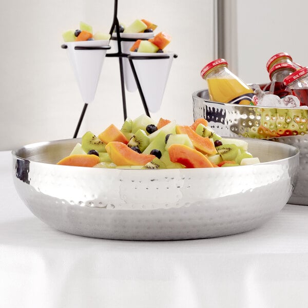 An American Metalcraft double wall hammered stainless steel bowl filled with fruit on a table.