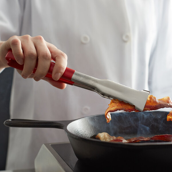 A chef using Vollrath VersaGrip tongs to cook bacon in a pan.