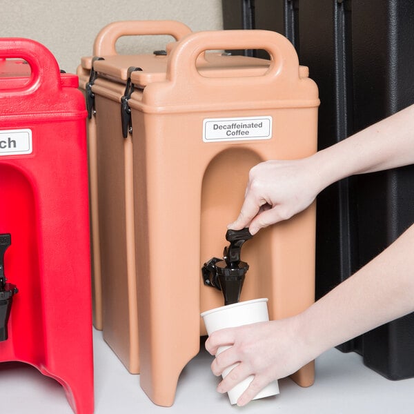 A hand pouring coffee into a Cambro insulated beverage dispenser.