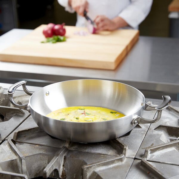 A chef using a Vollrath Miramar French Omelet Pan to cook in a kitchen.
