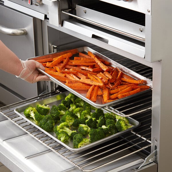 A person holding an Advance Tabco wire rim aluminum sheet pan filled with broccoli and carrots.