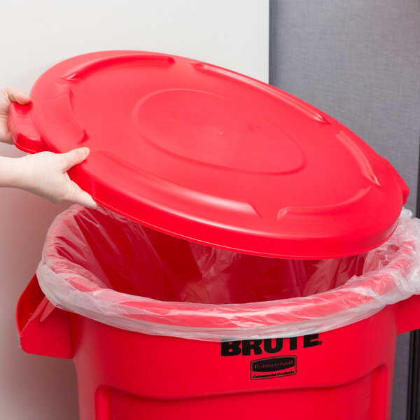 A hand putting a red Rubbermaid lid on a red trash can.