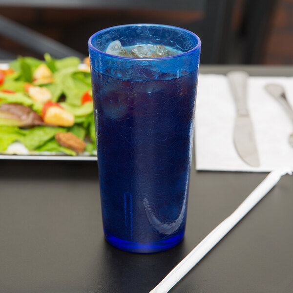 A blue cup with ice and a straw on a table with a salad.
