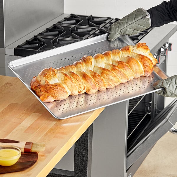 A person holding a Choice Wire in Rim Aluminum Perforated Bun / Sheet Pan with loaves of bread.