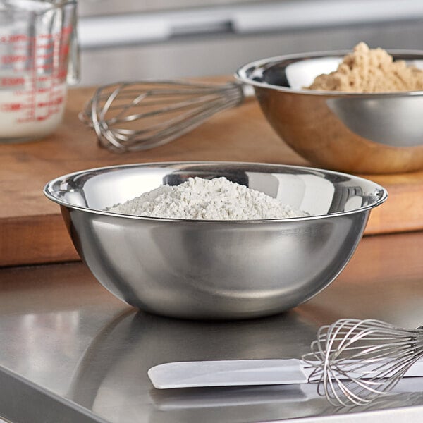 A Vollrath stainless steel mixing bowl with a whisk and flour on a counter.