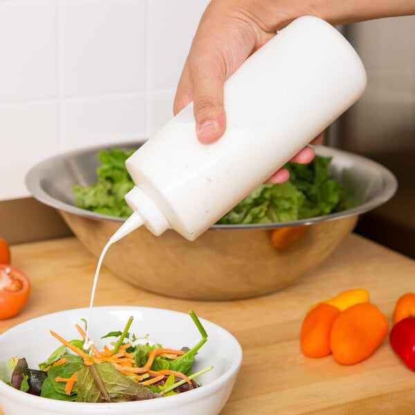 A person using a Tablecraft clear squeeze bottle to pour dressing onto a salad.