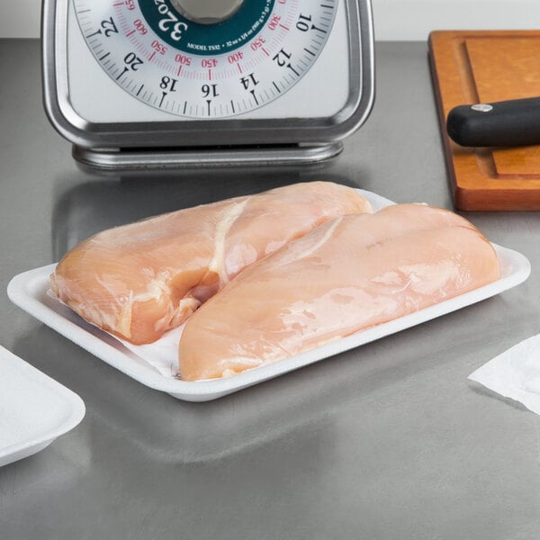 A white CKF foam meat tray holding two raw chicken breasts on a counter.