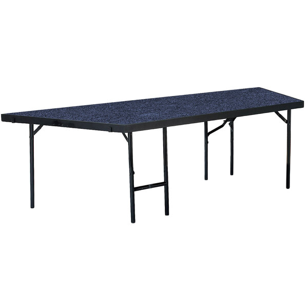 A National Public Seating portable stage pie unit with blue carpet on a rectangular table.