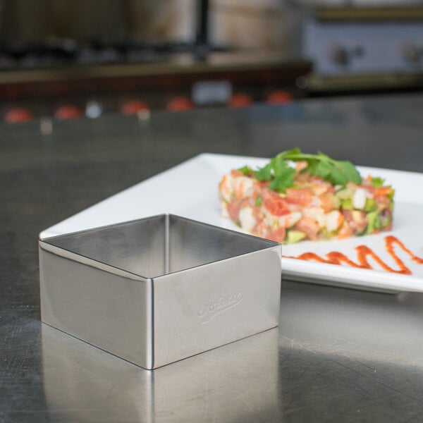 A stainless steel square mold on a plate.