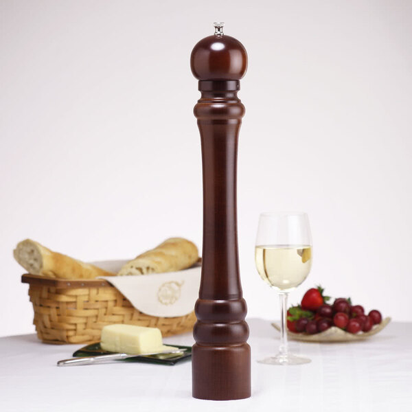 A close-up of a Chef Specialties Monarch Walnut Pepper Mill next to a glass of wine.