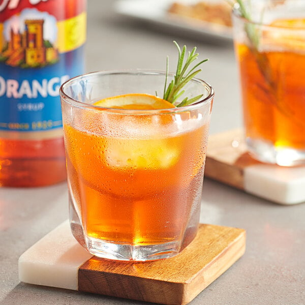 A glass of Torani orange liquid with a rosemary sprig on top.