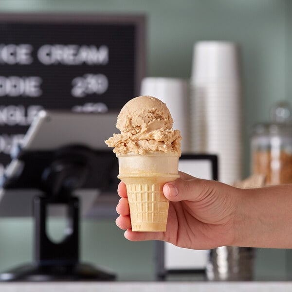 A hand holding a JOY flat bottom cake cone with ice cream.
