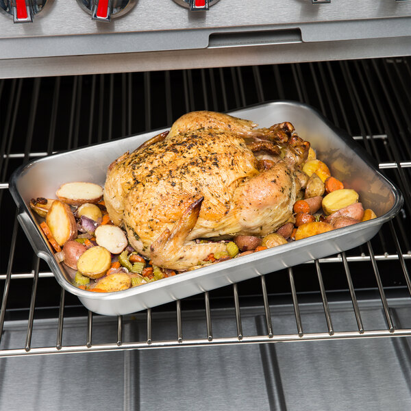 A roast chicken with vegetables in a Vollrath stainless steel roasting pan.