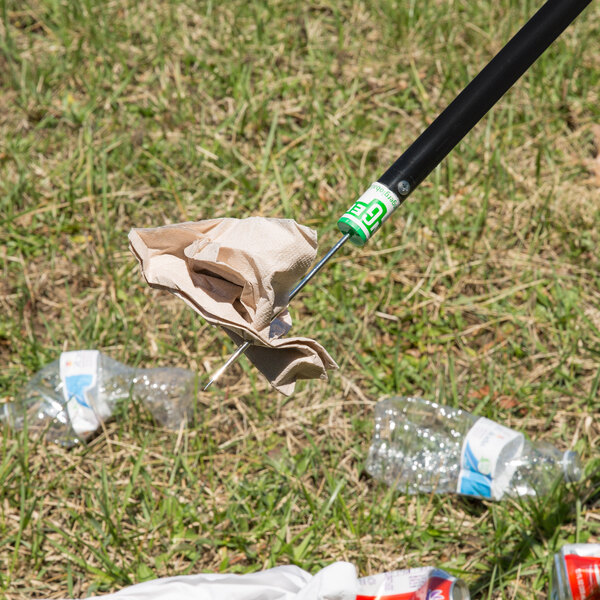 A Unger trash stick with a cloth on the end picking up a plastic bottle in the grass.
