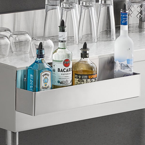 A Regency stainless steel speed rail on a counter with bottles and glasses.