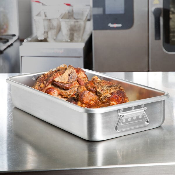 A Vollrath aluminum roasting pan with meat in it on a counter.