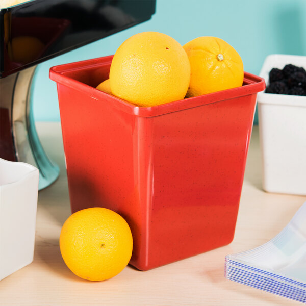 A red GET Sensation square crock filled with oranges on a white counter.