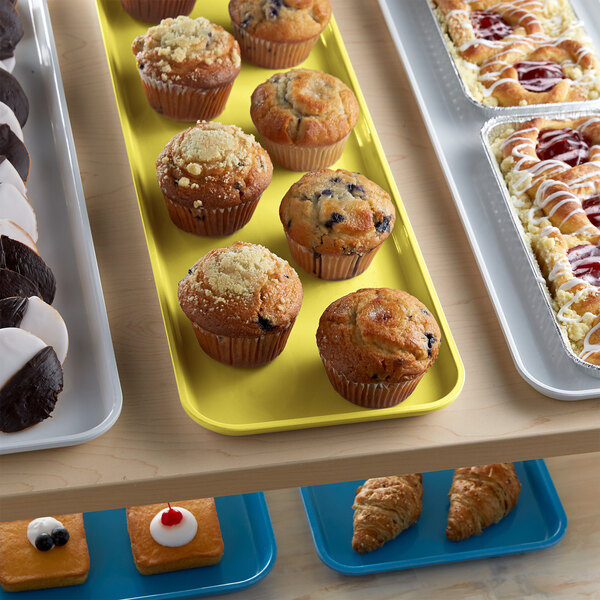 A yellow Cambro market tray holding muffins and pastries on a table.