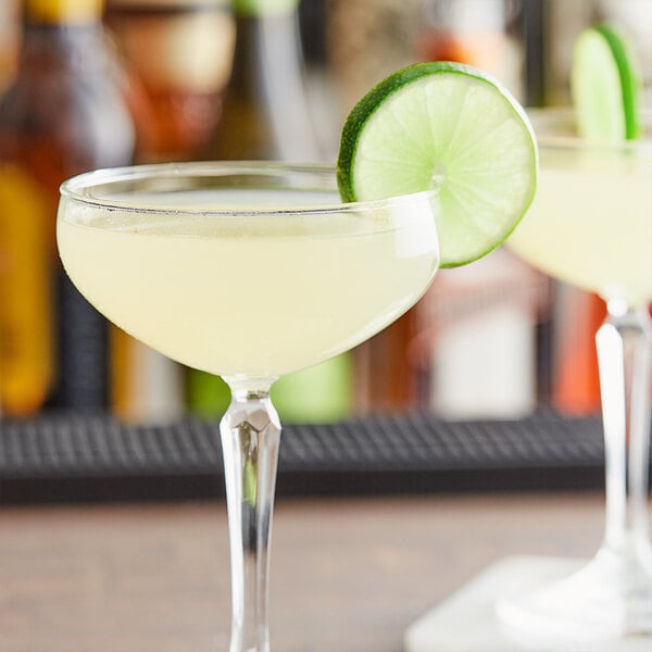 Two glasses of margaritas with a lime wedge in one and a glass of yellow liquid next to a lime slice.