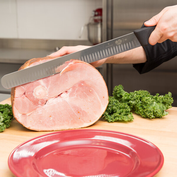A person using a Victorinox slicing knife to cut ham on a plate.