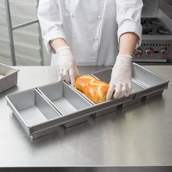 A person in white gloves putting a loaf of bread into a Chicago Metallic aluminized steel bread loaf pan.