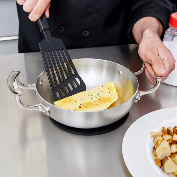 A chef using a Vollrath Miramar French omelet pan to cook eggs.