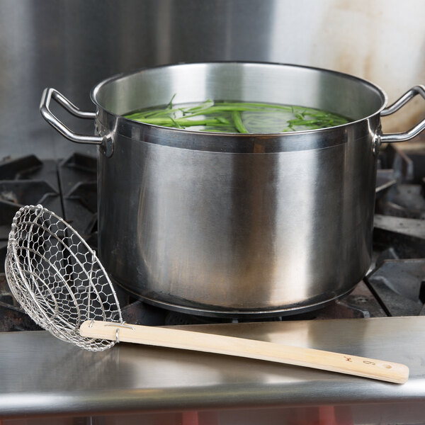 A pot of green beans on a stove with a bamboo-handled metal strainer.