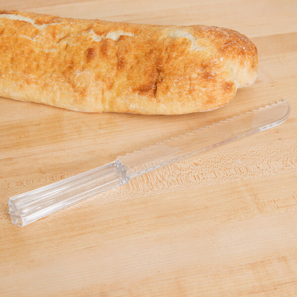 Clear plastic bread knife next to a loaf of bread on a table.