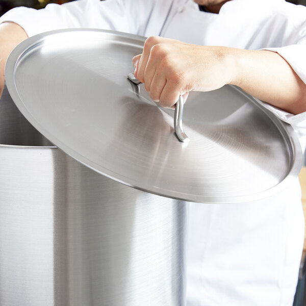 A chef using a Vollrath Optio metal pot lid to cover a large pot.