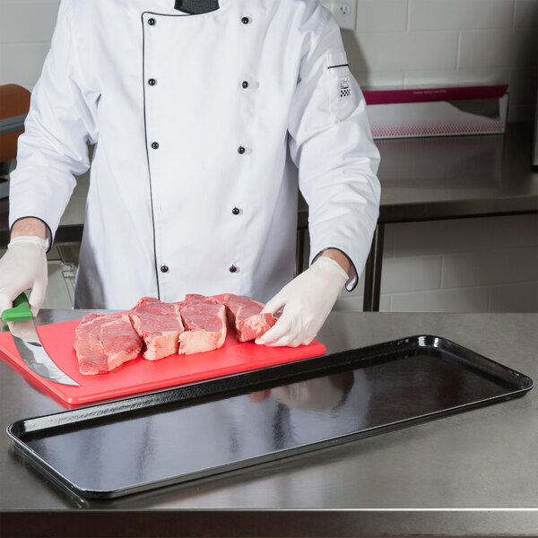 A chef cutting meat on a black Cambro market tray.