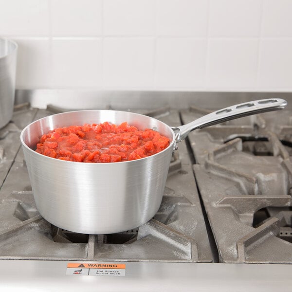 A Vollrath Wear-Ever aluminum sauce pan with red food on a stove.