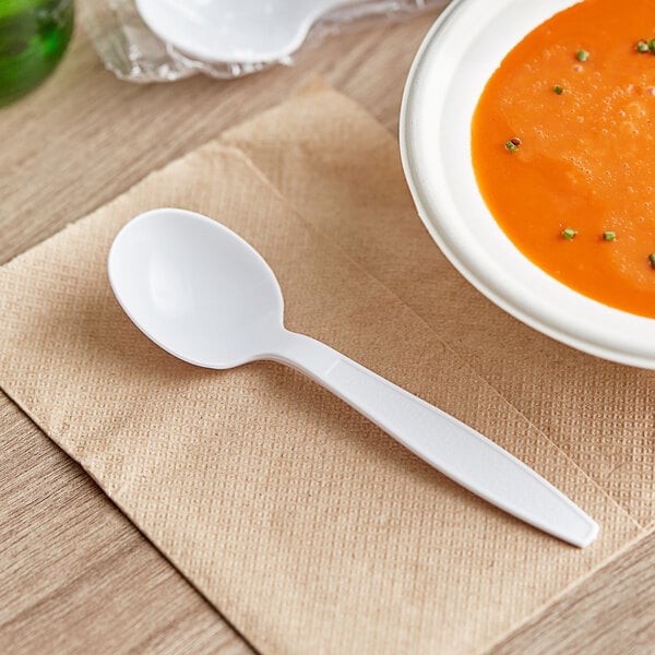 A white plastic soup spoon on a napkin next to a bowl of soup.