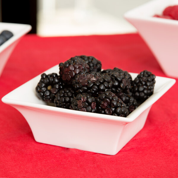 A bowl of blackberries in a white Arcoroc flared bowl on a red table.