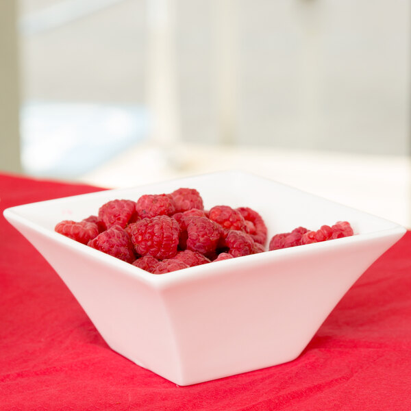 An Arcoroc flared bowl filled with raspberries on a red table.