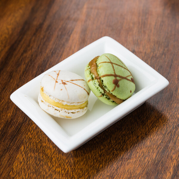 A white rectangular bowl filled with two macarons on a wood surface.