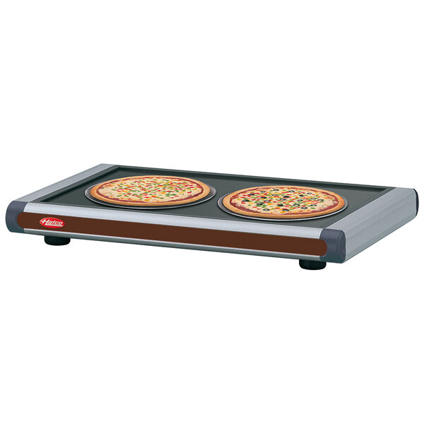 A Hatco heated shelf with two pizzas on a plate.