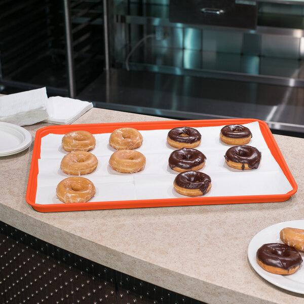 A Carlisle orange Glasteel bakery display tray on a counter with chocolate covered donuts.