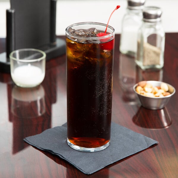An Anchor Hocking straight-sided zombie glass filled with a brown cocktail and topped with a cherry on a table.