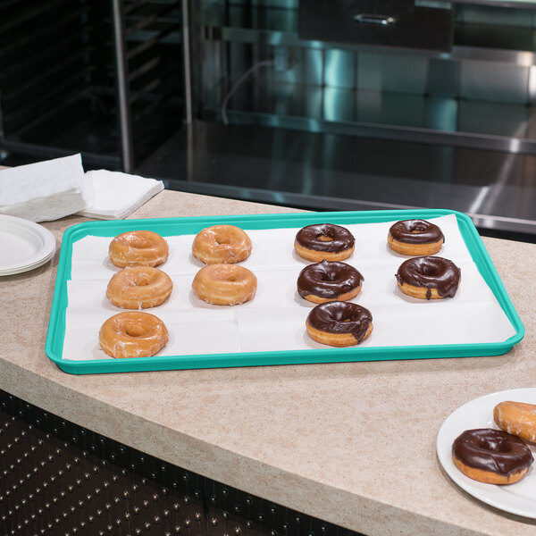 A Carlisle teal Glasteel bakery display tray of chocolate covered doughnuts on a counter.
