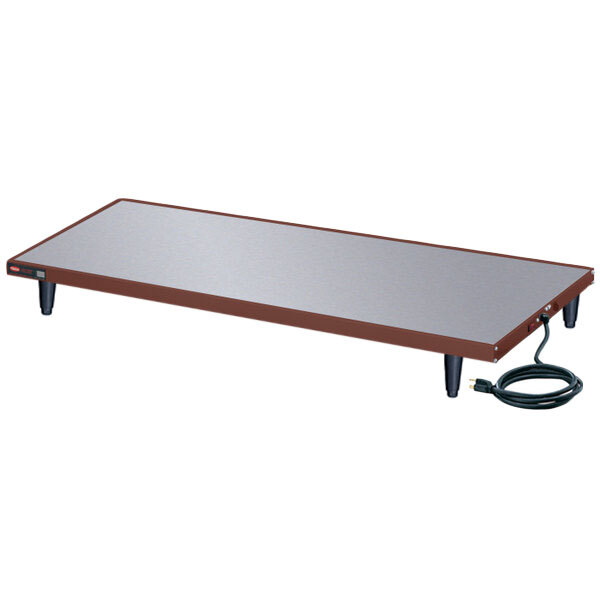 A rectangular copper heated shelf warmer on a table with a cord.